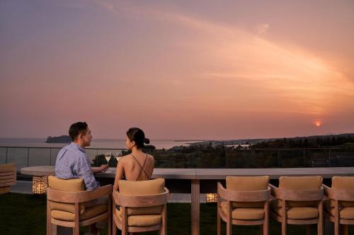 a man and a woman sitting at a table on a balcony with the sunset at JW Marriott Jeju Resort & Spa in Seogwipo