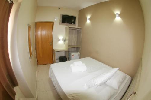 a small bedroom with a white bed with two pillows at Hotel Maria da Fé in Aparecida