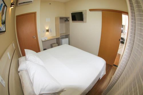 a small room with a white bed in it at Hotel Maria da Fé in Aparecida
