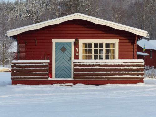 a red cabin with a blue door in the snow at Björkebo Camping in Stöllet