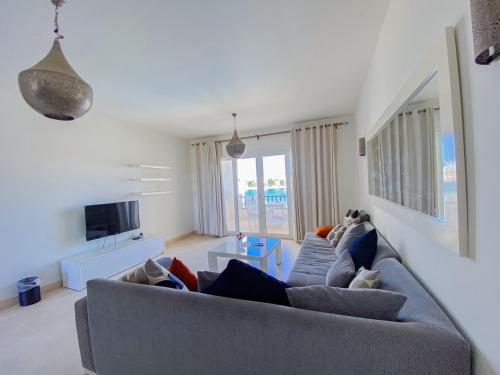 a living room with a gray couch and a tv at Nayah Stays, Joubal Lagoons flowery apartment in Hurghada