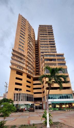 a tall building with a palm tree in front of it at Apto Frente al Mar Paseo Colon Puerto La Cruz in Puerto La Cruz