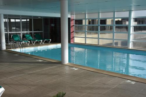 a swimming pool in a building with green chairs at Résidence Les Adrets de Peyragudes in Germ