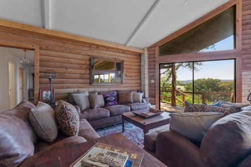 a living room with leather couches and a large window at Guadalupe Bluff Log Cabin in Kerrville