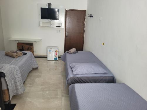 a room with two beds and a tv on the wall at Hospedaria São Benedito in Guararema