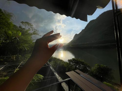 a persons hand looking out of a window at a lake at Little Rock Homestay in Phong Nha