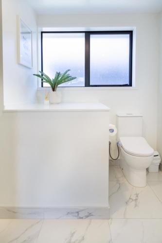 a white bathroom with a toilet and a window at Bright & Stylish 2BR Near Addington Park in Addington