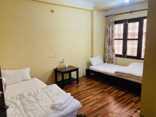 a room with two beds and a table and a window at Diya's Guest House - Family Environment in Bandīpur