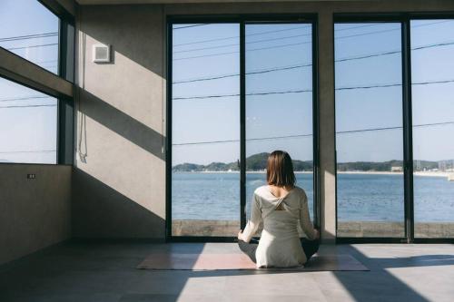 a woman sitting in a room looking out at the water at 糸島STAYｘCafe 海のみちひき-小富士あたり- in Itoshima