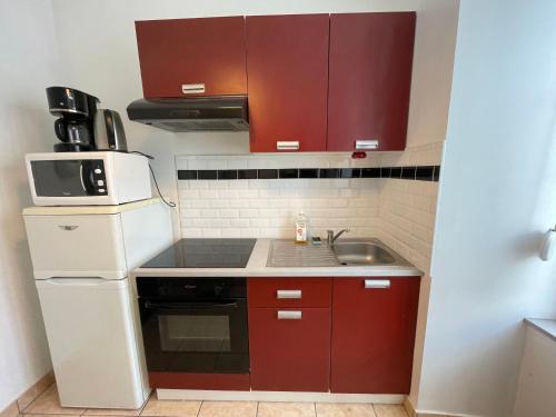une petite cuisine avec des armoires rouges et un évier dans l'établissement Studio chaleureux rez de chaussée, à Saint-Samson-sur-Rance