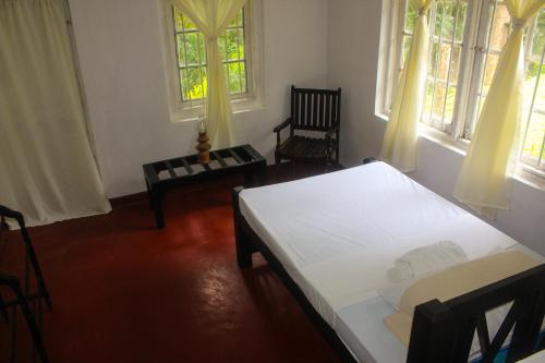 a bedroom with a bed and a chair and windows at HEYCOCK CEYLON HlLL in Gampola