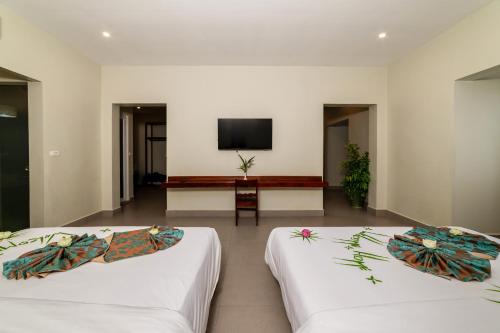 two beds in a room with a tv on the wall at Bayon Modern Residence in Siem Reap
