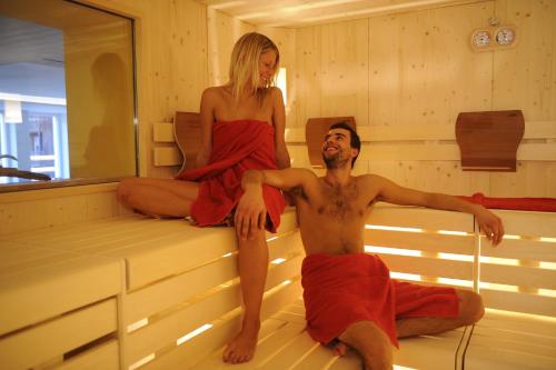 a man and a woman sitting in a sauna at Alpstyle Hotel Albolina Wellness & Beauty in Canazei