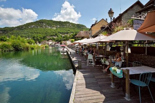 a river with people sitting at tables and umbrellas at Confort entre lac et montagne in Tresserves