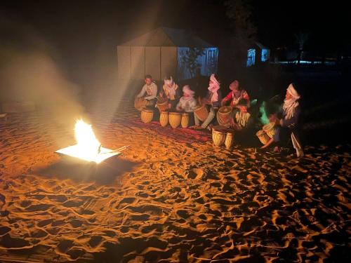 a group of people sitting around a fire on a beach at Khadija Desert Camp in Merzouga