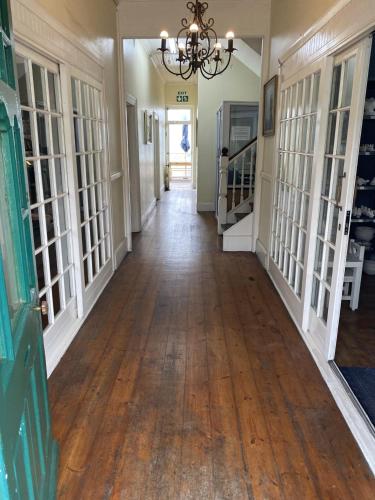an empty hallway in a house with a wooden floor and a chandelier at Green Door Guesthouse in Mossel Bay