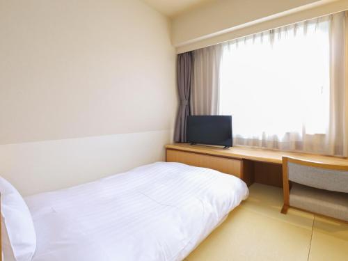 a hotel room with a bed and a desk and a window at Dormy Inn Tsu in Tsu