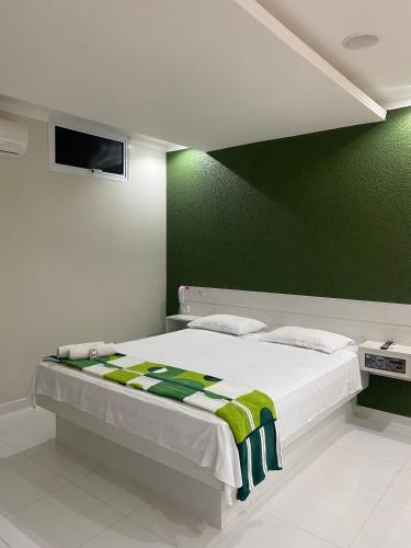 a bedroom with a white bed with a green wall at HOTEL E POUSADA ISIS in São Pedro