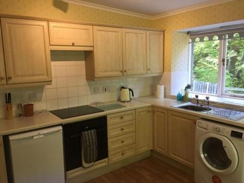 a kitchen with wooden cabinets and a sink and a dishwasher at The Delnashaugh in Ballindalloch