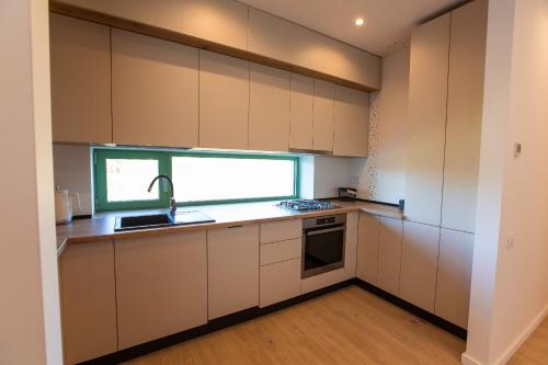 ブカレストにあるRoots Three - Modern Lakeview Apartmentの白いキャビネット、シンク、窓付きのキッチン
