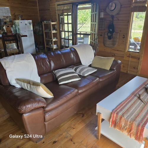 a brown leather couch with pillows on it in a room at Cabaña MISUEÑO in Punta Del Diablo