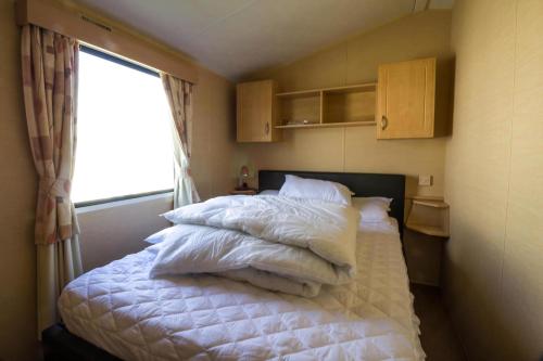 a bedroom with a bed with white sheets and a window at Lovely 6 Berth Caravan At Naze Marine Holiday Park In Essex Ref 17275C in Walton-on-the-Naze
