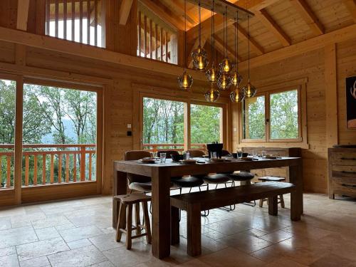 une salle à manger avec une table, des chaises et des fenêtres dans l'établissement Grand chalet 5 chambres, calme, proche commerces, babyfoot, appareils raclette et fondue - FR-1-624-165, à Verchaix