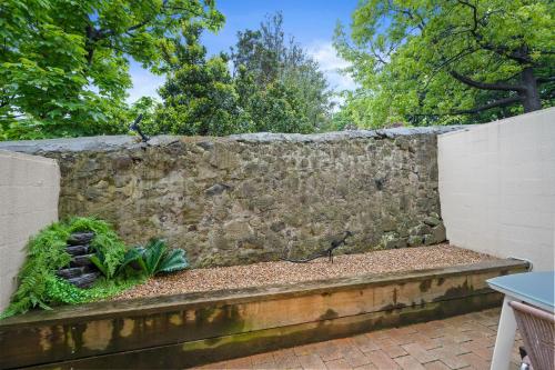 a stone retaining wall with a bench and plants at Hobart City Townhouse in Hobart
