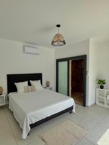 a white bedroom with a large bed and a chandelier at Les Roses du Désert in Étang-Salé