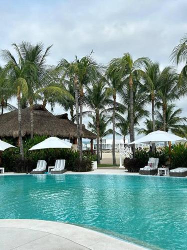 a swimming pool with chairs and umbrellas and palm trees at Casa de lujo con alberca y playa privada in Cruz de Huanacaxtle