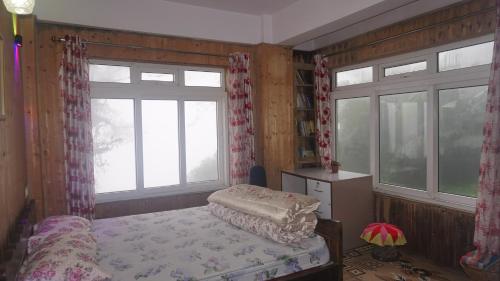 a bedroom with a bed and two windows at Tranquil Retreat Homestay in Ghum