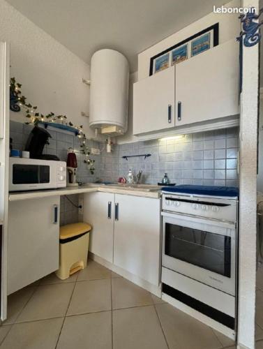 une cuisine avec des armoires blanches et un four à plaques de cuisson dans l'établissement Studio vue mer, au Cap d'Agde