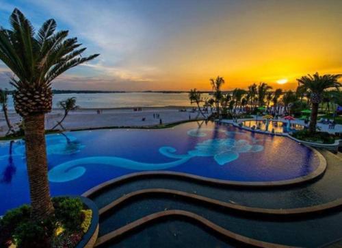 a resort pool with a palm tree and a sunset at Bay Point Love Bed Danga Bay in Johor Bahru