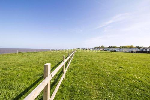 a white fence in a field next to the ocean at Stunning10 Berth Caravan With Decking At Broadland Sands In Suffolk Ref 20082Bs in Hopton on Sea