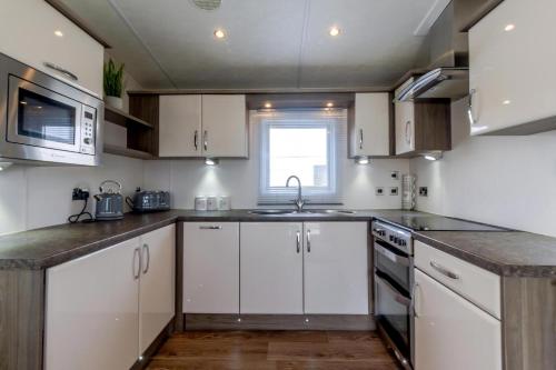 a kitchen with white cabinets and a sink and a microwave at Beautiful 6 Berth Caravan By The Beach In Suffolk Ref 40076Nd in Lowestoft