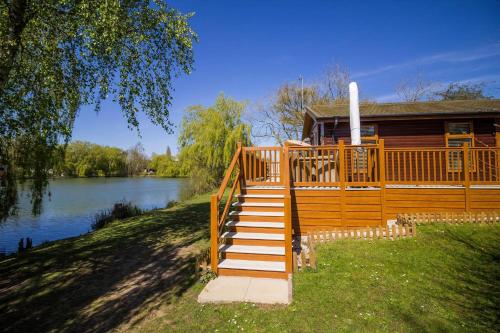 a wooden house with a staircase leading to a lake at Stunning Lodge With Free Wifi For Hire At Carlton Meres In Suffolk Ref 60013M in Saxmundham