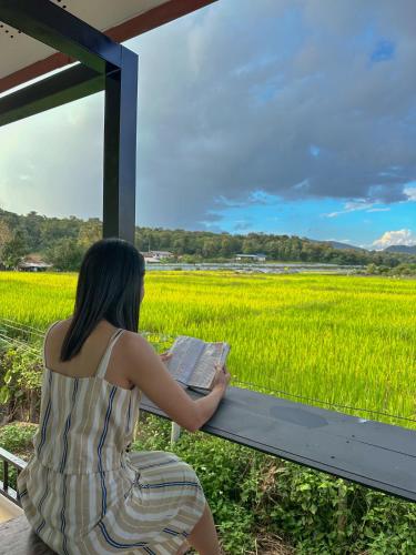 a woman sitting on a bench reading a book in front of a rice field at JJ and J Garden1 Pai in Pai