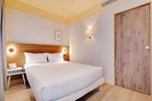 a bedroom with a white bed and a wooden door at Hôtel Cocoon in Saint-Ouen