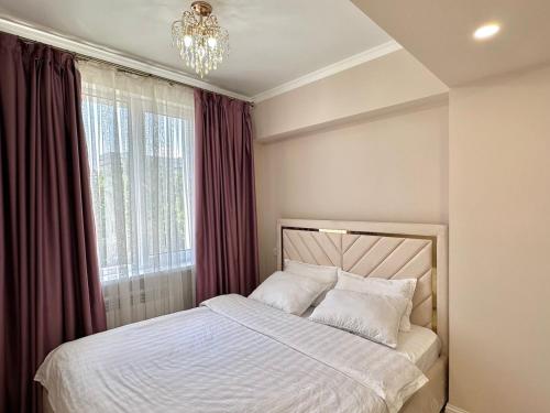 a bedroom with a bed with a chandelier and a window at Premium Residence, steps to center Arbat, drinking water as a gift in Almaty