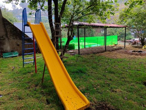 un parque infantil con un tobogán amarillo en el césped en Misty Valley Inn, en Kodaikanal