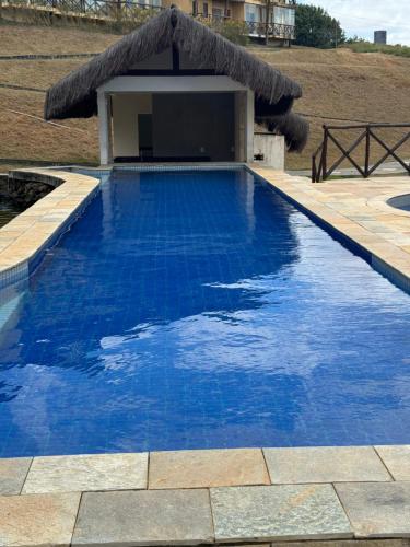 a blue swimming pool with a thatch roof at Sonhos da Serra Bananeiras - O melhor apartamento de bananeiras in Bananeiras