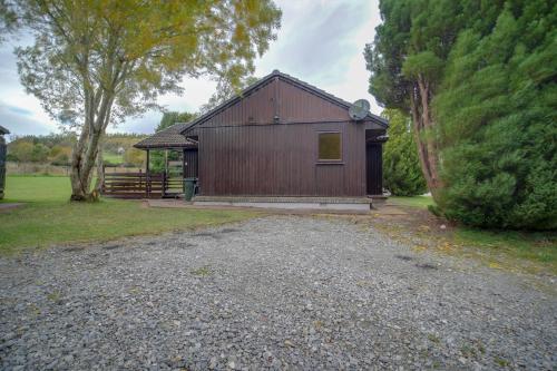 a brown building with a tree and a gravel driveway at Glenview Chalet Park in Inverness
