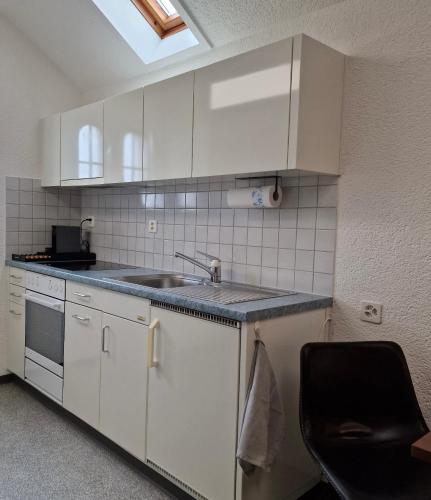 a kitchen with white cabinets and a sink and a chair at peaceful tiny house near forest in Rorschacherberg