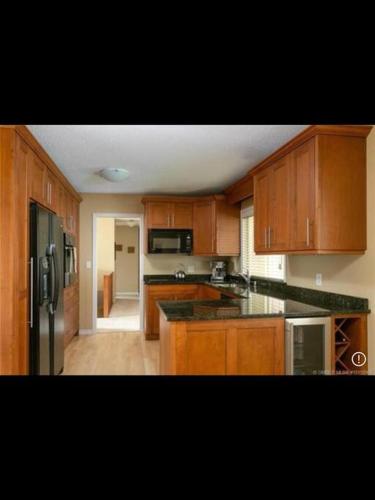 a kitchen with wooden cabinets and a black refrigerator at Spacious West Kelowna Home that is great for family, friends, or business trip! in West Kelowna