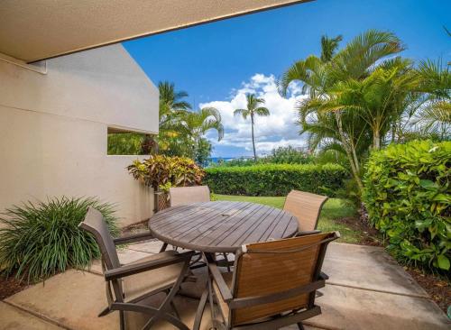 a wooden table and chairs on a patio with palm trees at Ho'omaha - Serene Kihei Condo in Maui Kamaole for Ocean Views and Relaxation in Wailea