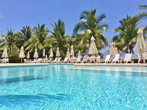 a swimming pool with chairs and umbrellas and palm trees at A pie de mar en zona hotelera, 1BR condo In Monarca Ixtapa, no pagas brazalete in Ixtapa