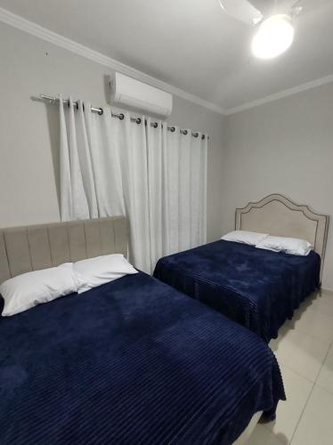 a bedroom with two beds with blue sheets and a window at Casa com garagem, ar condicionado, sala tv e jantar, cozinha completa e lavanderia in Taubaté