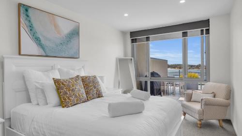 a white bedroom with a white bed and a chair at Waterfront On Market in Merimbula