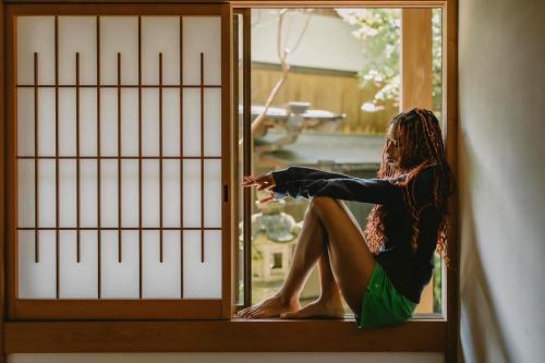 a woman sitting on a window looking outside at Uwanosora Bed&BBQ&Sauna in Shizuoka
