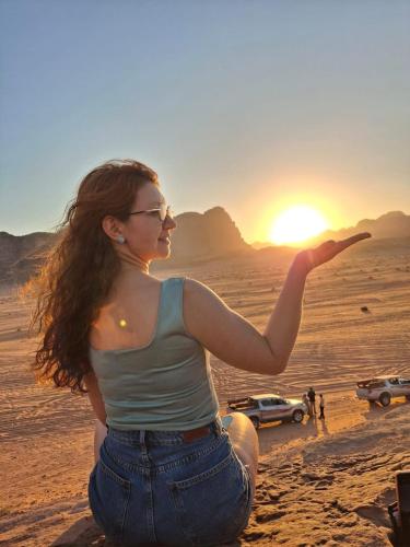 a woman sitting in the desert looking at the sunset at Dream Bedouin Life Camp Wadi Rum in Disah